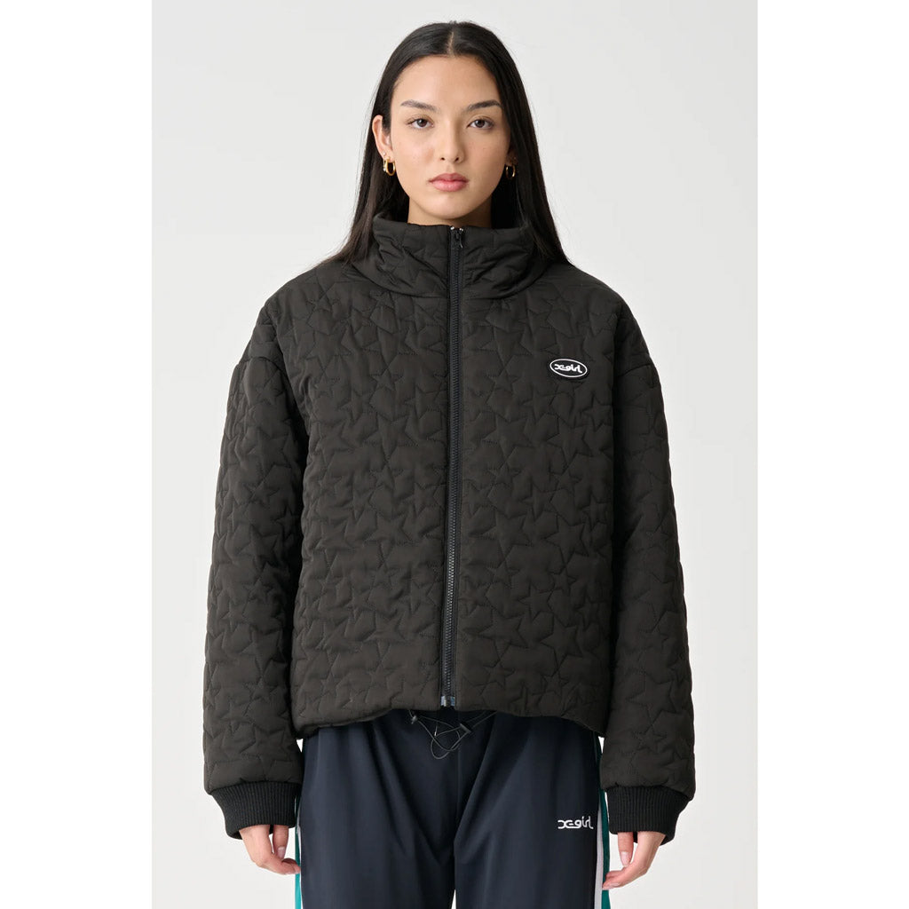 X-Girl Mills Puffer Jacket - Black. The Mills Puffer Jacket in Black is an oversized puffer jacket in a specialised all over quilted design. Featuring front zipper opening, high neck collar, adjustable bungee cord elastic at hem with toggles, side seam pockets & front chest rubber logo badge. Shop X-Girl with Pavement.